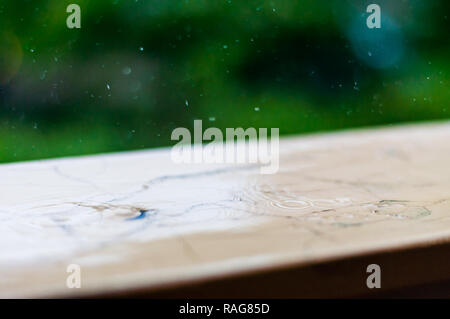 Sommer regen Regentropfen fallen auf Holz gemalten Griff der Balkon Geländer auf unscharfen Bäume Hintergrund Stockfoto