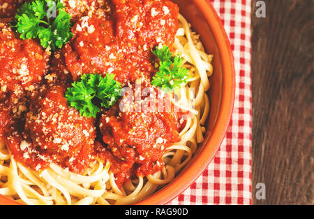 Linguine Nudeln mit Hackfleischbällchen in Tomatensauce und Petersilie in Ton Schüssel auf rustikalen Holzmöbeln Hintergrund. Ansicht von oben. Stockfoto