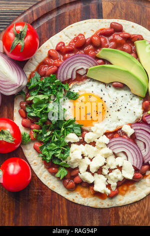 Huevos Rancheros frühstück Pizza mit Tomaten, Zwiebeln und Petersilie auf rustikalen Holzmöbeln Hintergrund. Ansicht von oben. Stockfoto