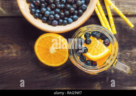 Detox Wasser mit Orange und Heidelbeeren im Glas auf rustikalen Holzmöbeln Hintergrund. Ansicht von oben. Stockfoto