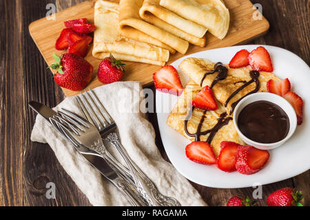 Frische, hausgemachte Pfannkuchen mit Erdbeeren und Schokolade Soße auf rustikalen Holzmöbeln Hintergrund. Stockfoto