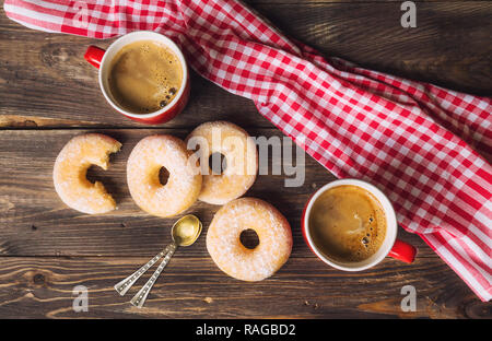 Zwei rote Becher mit Kaffee und Donuts auf der rustikalen Holzmöbeln Hintergrund. Ansicht von oben. Stockfoto