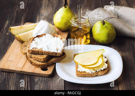 Toast mit Birne, ricotta Käse und Honig auf rustikalen Holzmöbeln Hintergrund mit Zutaten. Gesundes Frühstück. Stockfoto