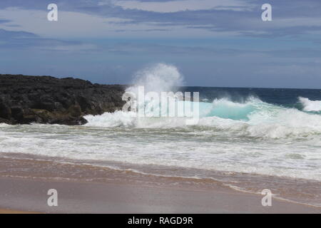 Ocean waves Spritzer Black Rock in der Nähe der Küste im Sommer an einen Strand in Kauai, Hawaii. Es gibt ein paar graue Wolken am Himmel. Stockfoto