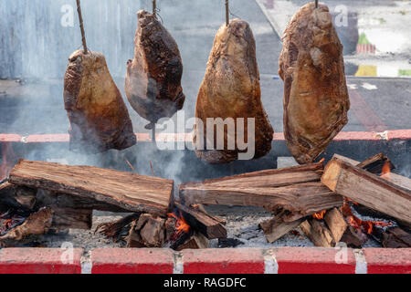 Vier große Stücke Fleisch am Spieß kochen über offenem Feuer mit Rauch und Flammen Stockfoto