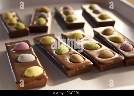 Osterschokoladentafeln, handgemacht und handwerklich hergestellt, Mini-Eier, die in Milchschokolade versinken. Deckenleuchte, die von den Schokoladentafeln leuchtet. Stockfoto