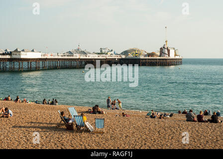 Blick auf den Strand von Brighton im späten Sommer Sonnenschein mit Urlaubern Entspannung am Strand einige in Liegestühlen mit Brighton Palace Pier im Hintergrund Stockfoto