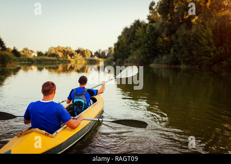 Junge Männer rudern Kajak auf dem Fluss bei Sonnenuntergang. Paar Freunde Spaß Kanu im Sommer Stockfoto