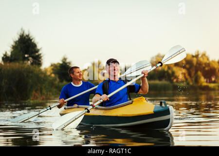 Junge Männer rudern Kajak auf dem Fluss bei Sonnenuntergang. Paar Freunde Spaß Kanu im Sommer Stockfoto