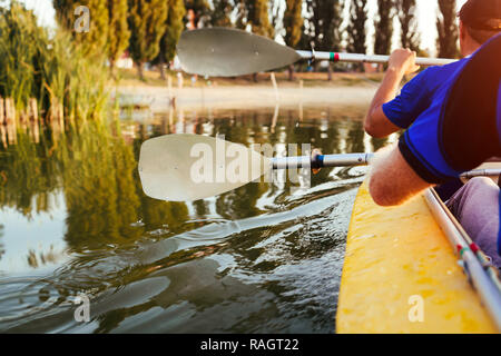 Junge Männer rudern Kajak auf dem Fluss bei Sonnenuntergang. Paar Freunde Spaß Kanu fahren im Sommer. Nahaufnahme des Paddles Stockfoto