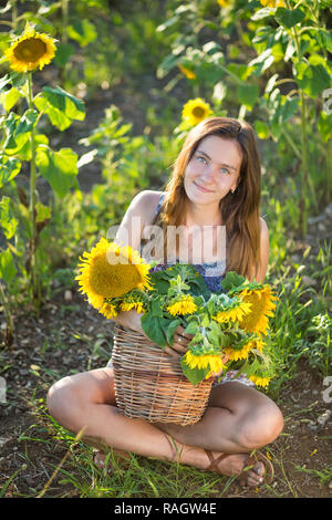 Süße Schöne junge Mädchen Dame Frau sitzt auf einem Feld mit großen Sonnenblumen. Brünette mit blauen Augen tragen bunte Kleidung italienischen Livorno sun Motorhaube Stockfoto