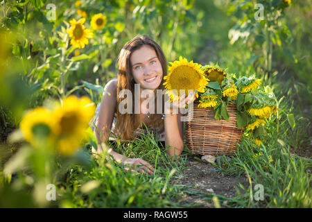 Süße Schöne junge Mädchen Dame Frau sitzt auf einem Feld mit großen Sonnenblumen. Brünette mit blauen Augen tragen bunte Kleidung italienischen Livorno sun Motorhaube Stockfoto