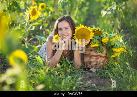 Süße Schöne junge Mädchen Dame Frau sitzt auf einem Feld mit großen Sonnenblumen. Brünette mit blauen Augen tragen bunte Kleidung italienischen Livorno sun Motorhaube Stockfoto