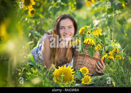 Süße Schöne junge Mädchen Dame Frau sitzt auf einem Feld mit großen Sonnenblumen. Brünette mit blauen Augen tragen bunte Kleidung italienischen Livorno sun Motorhaube Stockfoto