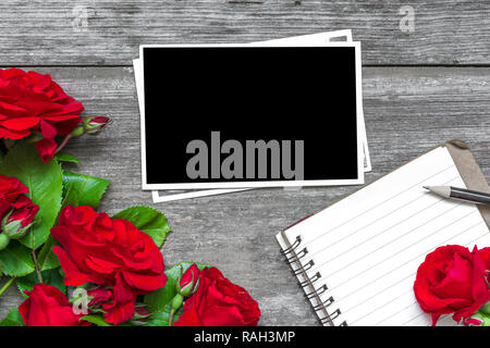 Leeren Bilderrahmen mit rote Rose blumen blumenstrauss und gefütterte Notebook mit rustikalen Holzmöbeln Hintergrund. top anzeigen. Mock up. Flach. Valentines Tag Hintergrund Stockfoto