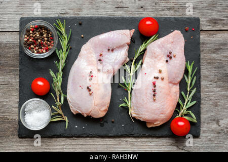 Raw Hähnchenschenkel mit Kräutern, Gewürzen und Tomaten cherry auf dunklem Schiefer Schneidebrett. Ansicht von oben. Lebensmittelzutat Stockfoto