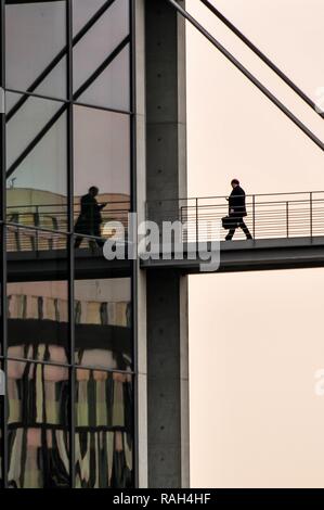 Unternehmer gehen über die Brücke in Richtung business Building, nobodz, Reflexion in der Glasfassade, mit Handy, Business und Executive Stockfoto
