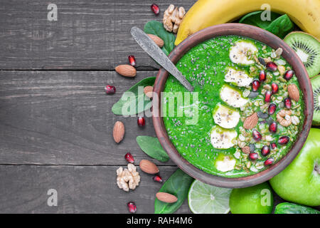 Grüne smoothie Schale aus Spinat, Brokkoli, Apfel, Zitrone und Kiwi garniert mit Müsli, Banane, Granatapfel, Kürbis und Chia Samen mit einem Löffel. nach oben Stockfoto