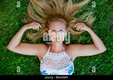 Portrait von blonde Frau in die Kamera schaut. Liegend auf dem Gras. Grüne Augen. Madrid, Spanien. Stockfoto