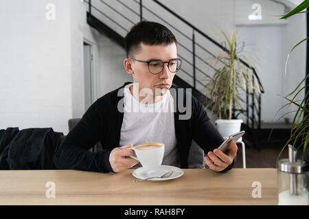 Sorgen junge Mann Lesen einer Nachricht mit schlechten Benachrichtigung auf modernen Smartphone im Cafe sitzen. Frustriert und verärgert hipster Kerl ansehen shocking Video im Blog auf zelluläre Stockfoto