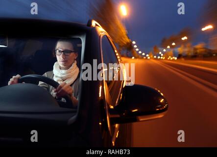 Junge Frau, die ihr Auto in der Nacht auf einer beleuchteten Straße Stockfoto