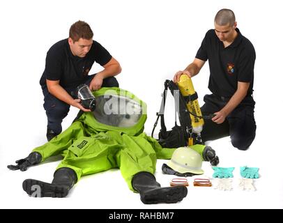 Feuerwehrmann helfen ein Kollege auf ein Chemikalienschutzanzug mit Luft aus einem Druckluft Atemschutzgeräte, Stockfoto