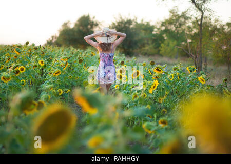 Süße Schöne junge Mädchen Dame Frau sitzt auf einem Feld mit großen Sonnenblumen. Brünette mit blauen Augen tragen bunte Kleidung italienischen Livorno sun Motorhaube Stockfoto