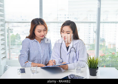 Ärztin spricht mit weiblichen Patienten im Krankenhaus Büro beim Schreiben auf die Patienten Gesundheit Datensatz in der Tabelle. Gesundheitswesen und medizinische Betreuung. Stockfoto