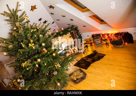 Weihnachtsschmuck im Studio, grosse natürliche Tanne Baum mit goldenen Kugeln, Schleifen und Schneeflocken, Kamin und Kerzen auf es und Braun gemütliche Ar Stockfoto