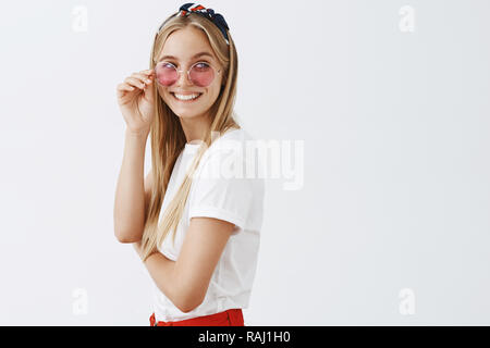 Sie weiß, was Stil ist. Portrait von selbstbewussten froh und glücklich modische Frau in trendigem Pink Sonnenbrille und Stirnband, rechts zu Lächeln an den Mann, der ihr Kompliment, berühren Gläser Stockfoto