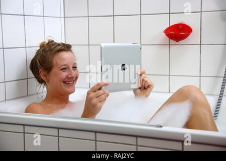 Junge Frau in einer Badewanne mit einem iPad, Tablet-PC, WLAN-Internetzugang Stockfoto