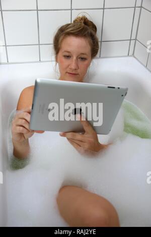 Junge Frau in einer Badewanne mit einem iPad, Tablet-PC, WLAN-Internetzugang Stockfoto