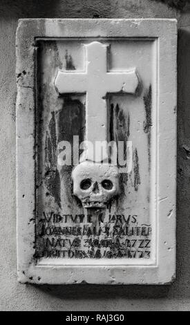 Schwarz und Weiß, schwere Platte mit Totenkopf und Kreuz auf urn Wand, St. Nikolaus Pfarrkirche, parrocchia San Nicolò, Altstadt Stockfoto