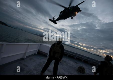 Mitglieder der Küstenwache Maritime Security Response Team West erwarten Extraktion durch die 129 Rettung Flügel in Tag- und Nacht-Zeit fast-rope Training auf dem Deck des Hornblower Geist in der San Francisco Bay, 5. Dezember 2018. Teammitglieder sind in fortgeschrittene Techniken mit Bundes-, Landes- und lokalen Partnern ausgebildet, um die Nation aus einer Vielzahl von wasserbasierten Bedrohungen zu schützen. U.S. Coast Guard Foto von Chief Petty Officer John Masson. Stockfoto