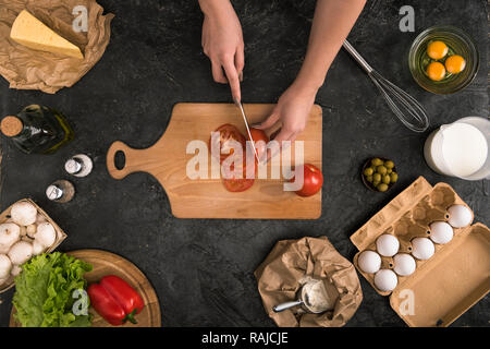 7/8-Ansicht von Frau hacken Tomaten auf Schneidebrett mit pizza Zutaten auf grauem Hintergrund Stockfoto