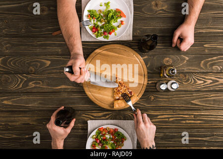 Blick auf die Männer, die Pizza mit Messer und Gabel an den hölzernen Tisch 7/8 Stockfoto