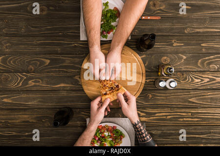 Blick auf die Männer, die pizza während der Mahlzeiten an den hölzernen Tisch 7/8 Stockfoto