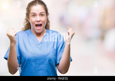 Junge brünette Mädchen mit Krankenschwester Arzt oder Chirurg gleichmäßig über isolierte Hintergrund überrascht Feiern und für den Erfolg mit erhobenen Armen erstaunt und Stockfoto