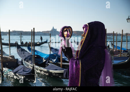 Venedig, Italien - 10. Februar 2018: Frau in Gold und Purpur Kostüm Maske Venedig Karneval stand vor der Gondeln und Suchen in der m Stockfoto