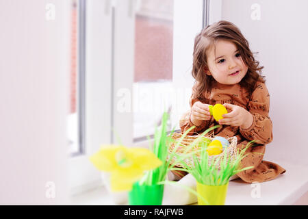 Mädchen in einem schönen Kleid malt Eier für das Osterfest Korb in der Nähe der Fenster Stockfoto