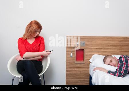 Junge Frau mit Handy, während Ihr Partner schläft Stockfoto