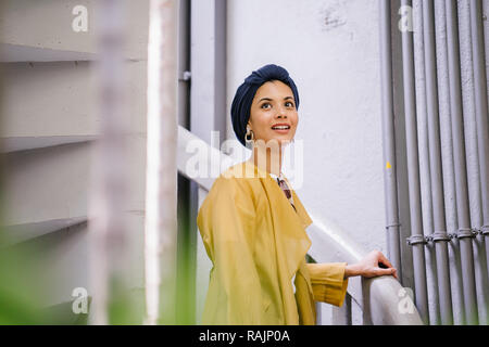 Mode portrait einer jungen, schönen arabischen Nahen Ostens Frau in einem eleganten Pastellfarben Outfit und Turban hijab stehen auf einer Wendeltreppe. Stockfoto