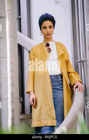Mode portrait einer jungen, schönen arabischen Nahen Ostens Frau in einem eleganten Pastellfarben Outfit und Turban hijab stehen auf einer Wendeltreppe. Stockfoto