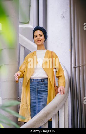 Mode portrait einer jungen, schönen arabischen Nahen Ostens Frau in einem eleganten Pastellfarben Outfit und Turban hijab stehen auf einer Wendeltreppe. Stockfoto