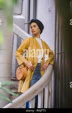 Mode portrait einer jungen, schönen arabischen Nahen Ostens Frau in einem eleganten Pastellfarben Outfit und Turban hijab stehen auf einer Wendeltreppe. Stockfoto