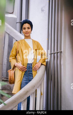 Mode portrait einer jungen, schönen arabischen Nahen Ostens Frau in einem eleganten Pastellfarben Outfit und Turban hijab stehen auf einer Wendeltreppe. Stockfoto