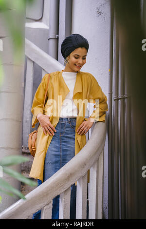 Mode portrait einer jungen, schönen arabischen Nahen Ostens Frau in einem eleganten Pastellfarben Outfit und Turban hijab stehen auf einer Wendeltreppe. Stockfoto