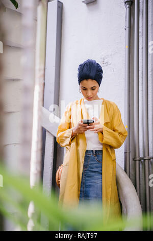 Mode portrait einer jungen, schönen arabischen Nahen Ostens Frau in einem eleganten Pastellfarben Outfit und Turban hijab stehen auf einer Wendeltreppe. Stockfoto