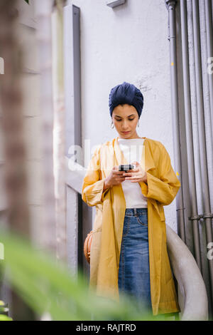 Mode portrait einer jungen, schönen arabischen Nahen Ostens Frau in einem eleganten Pastellfarben Outfit und Turban hijab stehen auf einer Wendeltreppe. Stockfoto