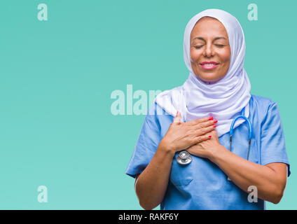 Mittleres Alter älteren arabischen Krankenschwester Frau, tragen, Hijab über isolierte Hintergrund lächelnd mit der Hand auf der Brust mit geschlossenen Augen und dankbare Geste auf das Gesicht. Uhr Stockfoto